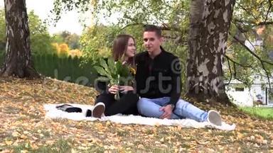 一对年轻夫妇坐在秋天公园的白色床单上